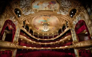 View of a large audience hall over several levels, red chairs and many gold decorations.