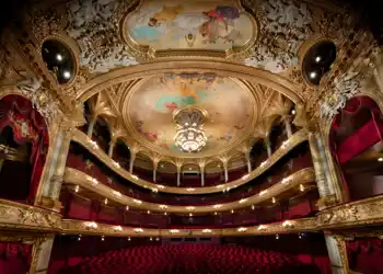 View of a large audience hall over several levels, red chairs and many gold decorations.