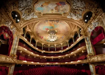 View of a large audience hall over several levels, red chairs and many gold decorations.