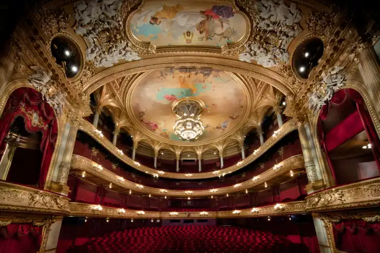 View of a large audience hall over several levels, red chairs and many gold decorations.