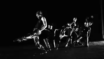 Black and white image of several dancers moving against a dark background.