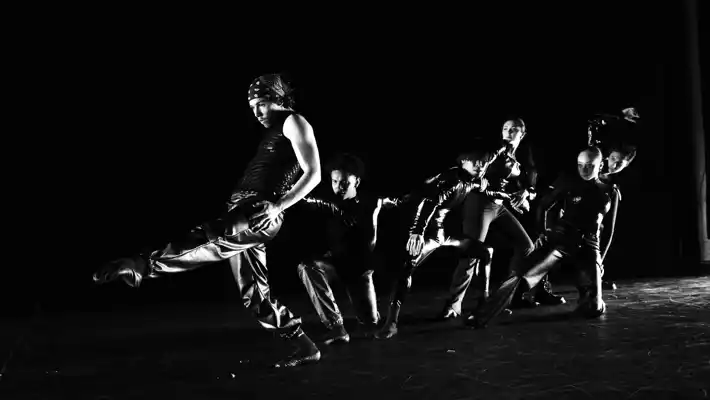 Black and white image of several dancers moving against a dark background.