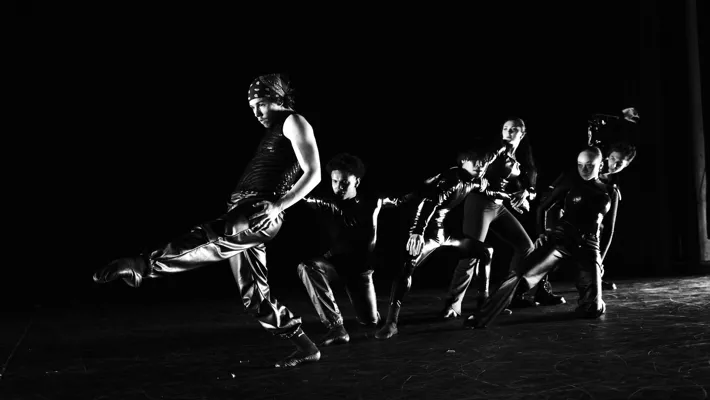 Black and white image of several dancers moving against a dark background.