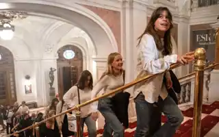 People walk on a staircase in an elegant building with arches and chandeliers.