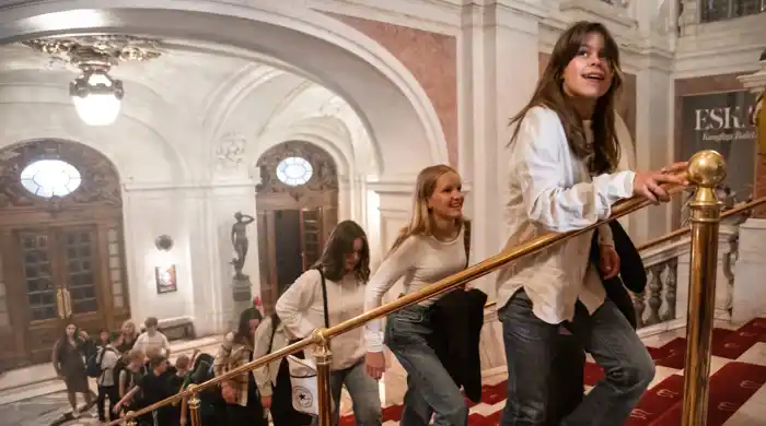People walk on a staircase in an elegant building with arches and chandeliers.