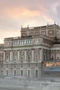 A large house by a stream, a church in the background, a light fog around the buildings.