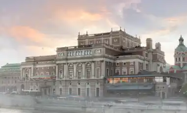 A large house by a stream, a church in the background, a light fog around the buildings.