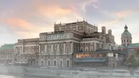 Ett stort hus vid ett vattendrag, en kyrka i bakgrunden, en lätt dimma runt byggnaderna.