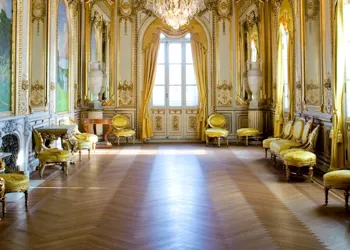 A room with yellow furniture along the walls, large windows where sunlight streams through.