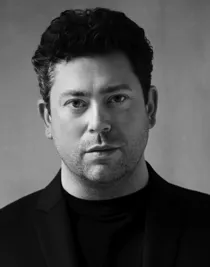 A close-up of a dark-haired man in a dark suit.