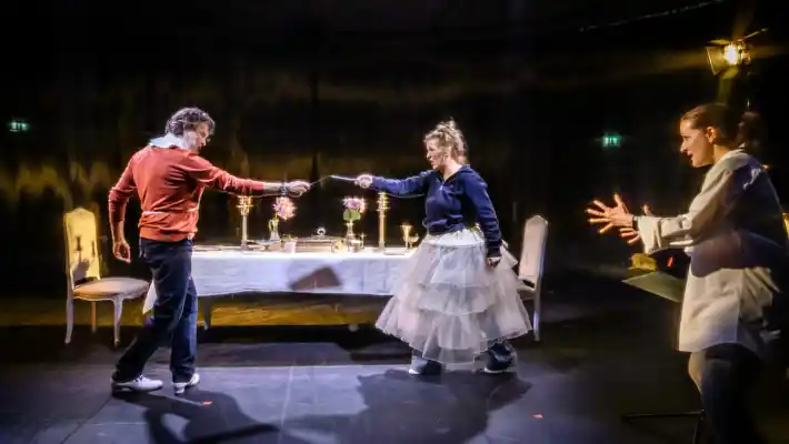 A woman and a man are pointing at each other, with another woman next to them who appears to be giving them instructions.