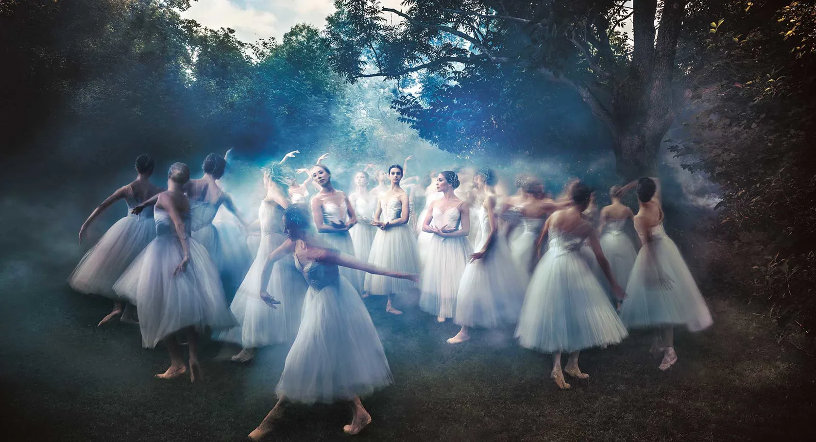 Ballet dancers in white tulle skirts surrounded by mist in a forest grove, create a dreamlike atmosphere.