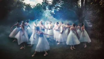 Ballet dancers in white tulle skirts surrounded by mist in a forest grove, create a dreamlike atmosphere.