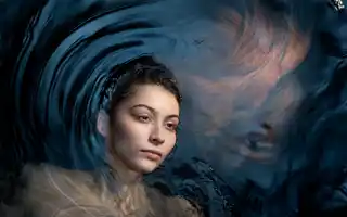 A dark-haired woman looks at us, she is half submerged in dark water.