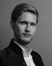 A close-up of a fair-haired man with a white shirt and dark jacket.