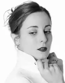 Close-up of a woman in a white shirt, the collar is turned up and she is holding it with both hands.