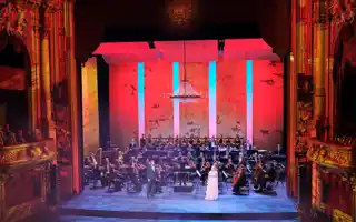 En vackert upplyst scen, omgärdad av gulddekor, med orkester och sångare i förgrunden.