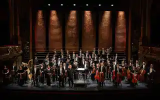 Many musicians stand spread out on a large stage.