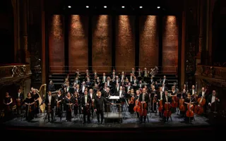 Many musicians stand spread out on a large stage.