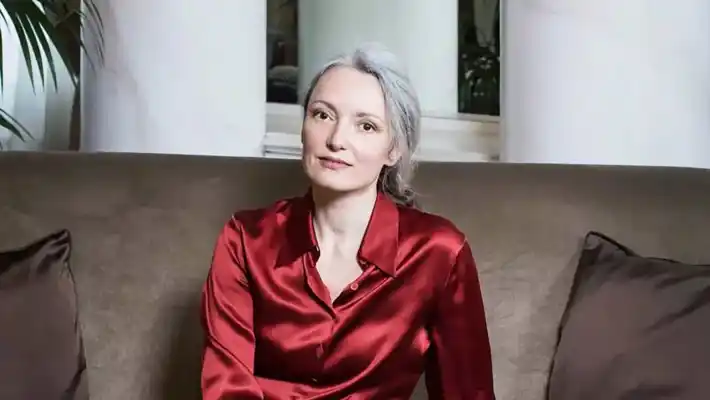 A woman in a red blouse sits on a brown sofa.