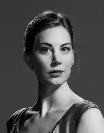 Close-up of a woman with her hair up, she is wearing a sleeveless silk top.