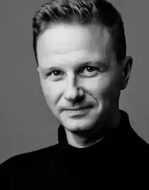 Close-up of a blond man wearing a dark polo shirt.