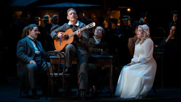 A group of people sitting around a table with a man playing the guitar.