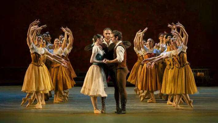 On a stage, you see a young couple in the middle, surrounded by several female dancers.