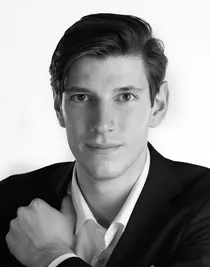 A close-up of a man wearing a white shirt and dark jacket.