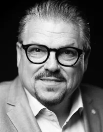 Close-up of a man with glasses: he is wearing a jacket and an unbuttoned shirt.