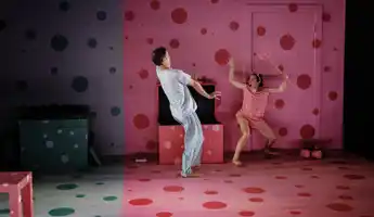 A girl with a trident and devil horns scares a boy on a stage.