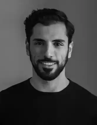 Porträttbild av en leende mörkhårig man med skägg, iklädd en mörk tröja.