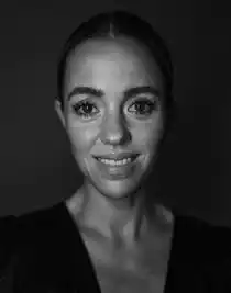 A close-up of a smiling woman, her hair is slicked back and she is wearing a dark low-cut top.