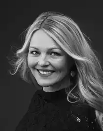 Close-up of blonde woman with bushy hair smiling at camera.