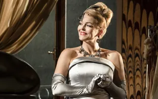 A smiling woman with updo hair, a small veil covering her face, a silver dress and long gloves.