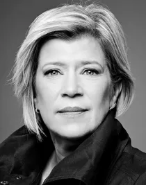 A close-up of a woman with a short blonde hair, her dark collar is turned up.