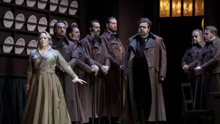 A group of people stand in a kitchen-like environment, plates lined up on the wall behind them.