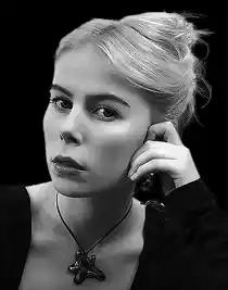 A woman with her hair up, leaning her face against her hand, the background is dark.