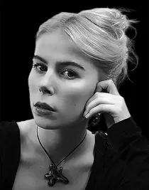 A woman with her hair up, leaning her face against her hand, the background is dark.