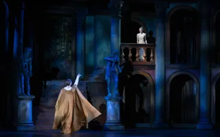 A man, with an arm stretched out, is standing below a balcony, on the balcony stands a young woman.