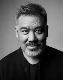 A close-up of a slightly smiling, bearded man dressed in dark clothes.