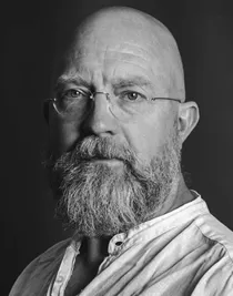 Close-up of a man wearing glasses, he is dressed in a light linen shirt.