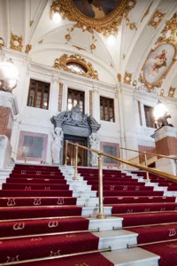 A large, wide staircase with red carpet leads up into an ornate stairwell.