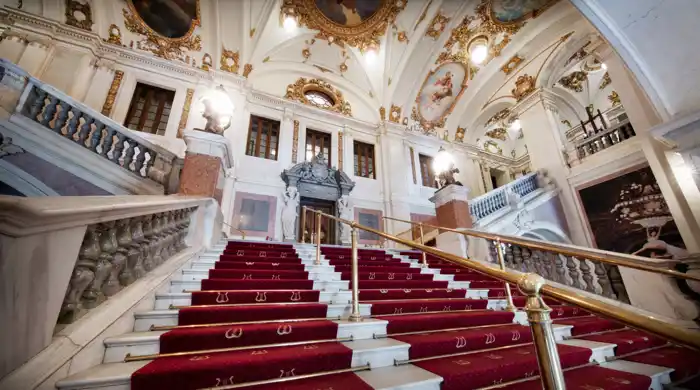 A large, wide staircase with red carpet leads up into an ornate stairwell.